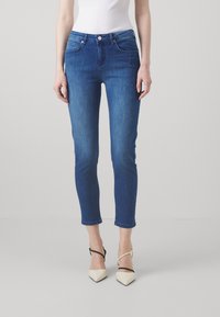 Jeans ajustados de mezclilla azul oscuro con una textura suave, cintura de altura media y longitud recortada, combinados con tacones crema de punta afilada.