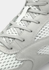 Gray athletic shoe with mesh panels and suede accents. Features flat gray laces and a textured sole design. Close-up view of detailing.