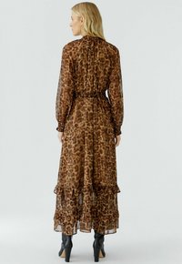 Lange, bruine jurk met luipaardprint, een gerimpelde zoom, gathers mouwen en een strik in de taille. Draagt het met zwarte hakken.