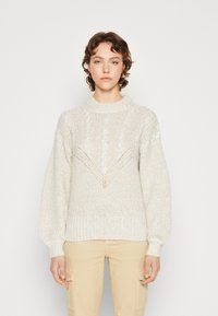 Lys beige strikket sweater med høj hals, tekstureret mønster og ballonærmer. Har et V-formet design på forsiden.