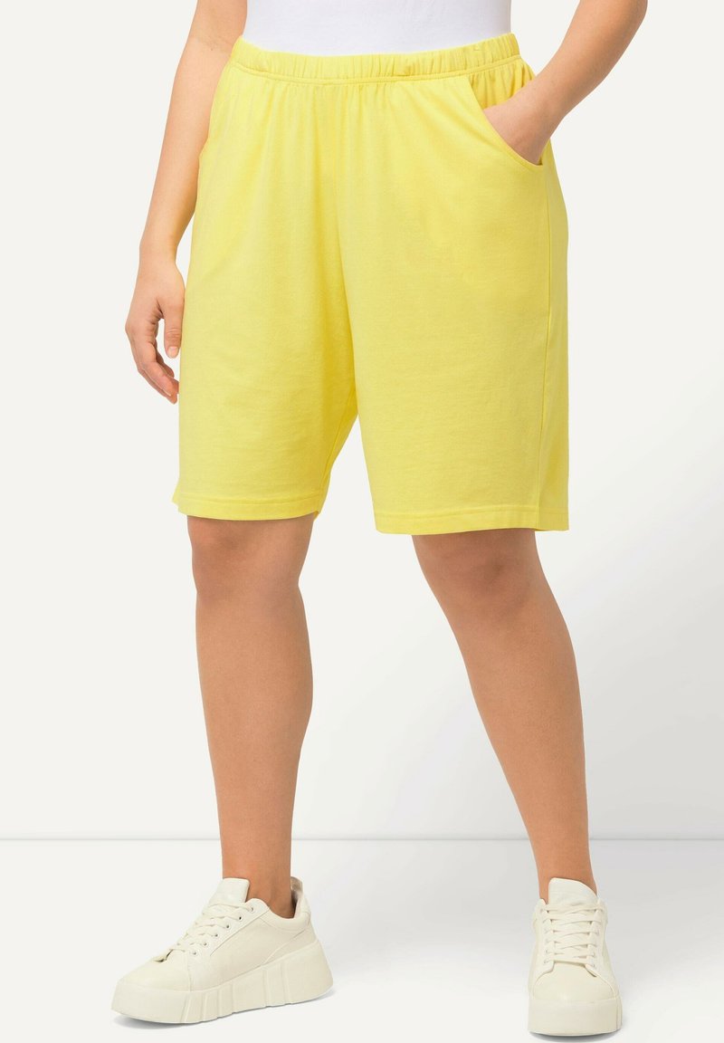 Žluté bavlněné šortky s elastickým pasem a bočními kapsami. Design má střih po kolena a jemnou texturu.