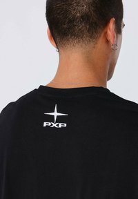 Camiseta negra con un logotipo bordado en blanco que dice "PXP" y un gráfico de estrella en la parte superior de la espalda. Tejido suave y liso.