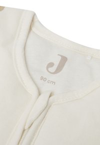 Cream-colored infant garment with a soft texture, featuring a front zipper and a label printed with the letter "J" and size 90 cm.