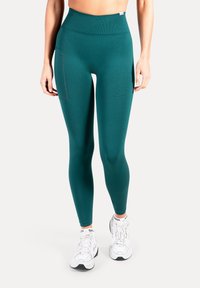 Leggings taille haute couleur sarcelle en tissu lisse et extensible, dotés d'une poche latérale et d'une ceinture côtelée, associés à des baskets blanches.