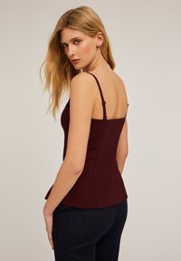 Burgundowa dopasowana koszulka na ramiączkach z cienkimi regulowanymi paskami, z falbaną u dołu i gładką fakturą. Widok z tyłu podkreśla eleganckie kroje.
