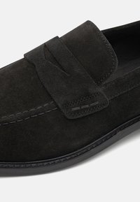 Mustad nubukist loaferid pompoonide aksendiga, ümarate varvastega, õmblusdetailidega ja kummist tallaga, mis tagab haarduvuse.