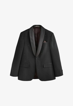 Uomo che sistema la manica di una giacca da smoking nera con rever in raso e piccolo motivo a puntini lucidi sopra una camicia bianca.