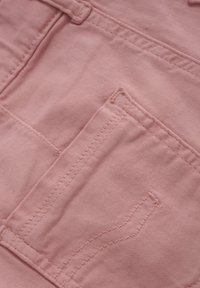 Helles rosa Denim-Stoff mit sichtbaren Nähten und einem kleinen Taschendetail. Texturierte Oberfläche mit einem weichen, baumwollähnlichen Aussehen.