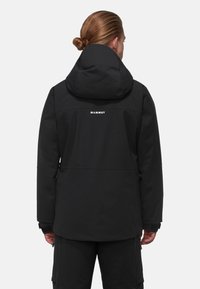 Black waterproof jacket with a hood, minimalist design, and visible white "MAMMUT" logo on the back. Features long sleeves and zippers.