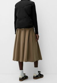 Black padded vest over a long, pleated brown skirt. Sneakers with black detailing and white socks. Smooth fabric with a clean design.