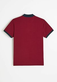 Czerwona koszulka polo z granatowym kołnierzem, krótkimi rękawami i teksturowanym wzorem na całej powierzchni. Zaprojektowana bez widocznych zapięć i ozdób.