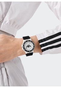 Must karbonrihmaga kell valge ümmarguse korpusega, musta krooniga ja selgete numbriliste märkidega valgel kellaseinal. Hõbedased tunni- ja minutinäidikud.