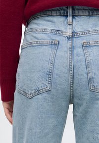 Vue de dos d’une personne portant un jean en denim bleu clair avec deux grandes poches arrière et un pull rouge à manches longues.