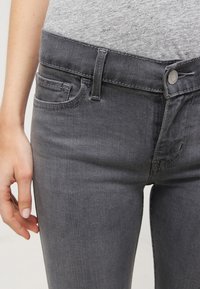Jeans de mezclilla gris con un diseño ajustado. Las características incluyen un cierre de botón, presillas para cinturón y bolsillos frontales, con una textura suave.