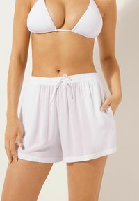 Bañador blanco hecho de tela ligera, con una cinturilla elástica con cordón y bolsillos laterales. Textura suave, diseño casual.