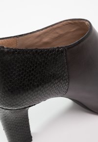 Chaussure à talon haut noire avec un motif texturé en forme d'écailles sur le talon et l'arrière, cuir lisse sur les côtés et doublure intérieure beige douce.