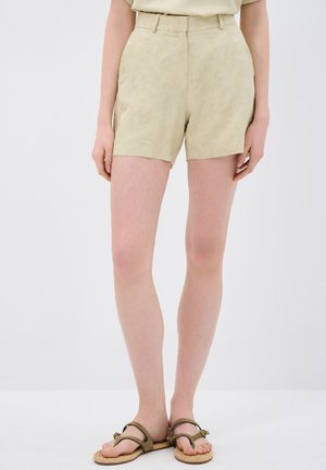Pantalones cortos beige claros con un patrón texturizado sutil, de cintura alta y ajuste entallado, combinados con sandalias planas marrones.