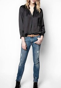 Zwarte satijnen blouse met een kraag, gecombineerd met versleten blauwe skinny jeans en zwarte enkellaarzen. Zichtbare riemdetail.