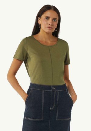 Olivegrünes T-Shirt mit kurzen Ärmeln, Rundhalsausschnitt und Ziernaht in der Mitte, kombiniert mit einem dunklen Jeansrock mit weißen Nähten.