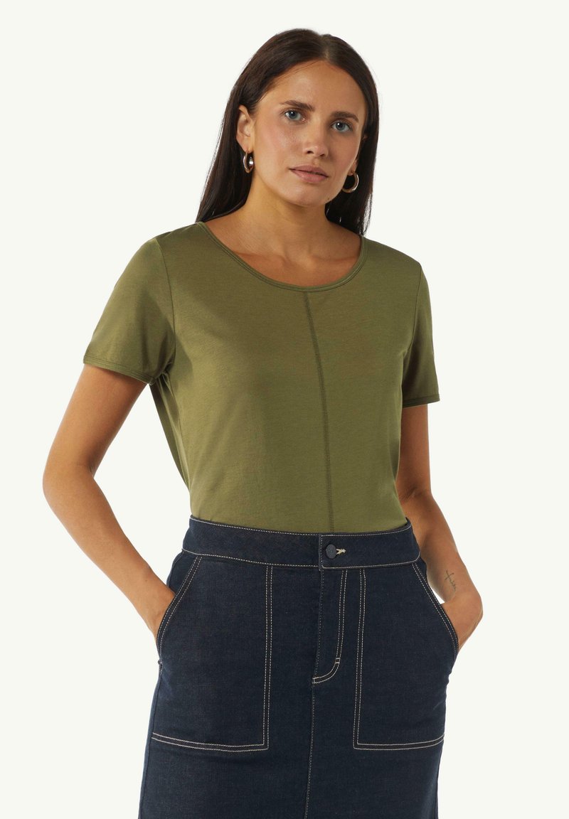 Olivegrünes T-Shirt mit kurzen Ärmeln, Rundhalsausschnitt und Ziernaht in der Mitte, kombiniert mit einem dunklen Jeansrock mit weißen Nähten.