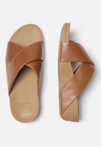 Bruine leren slidesandalen met kruisbanden, een gestructureerde zool en een lage, gevormde platform voor comfort. Logo in de zool gedrukt.