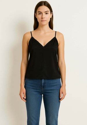 Camisola nera in satin con sottili spalline regolabili e scollatura a V. Presenta un bordo ondulato lungo la scollatura e l'orlo. Abbinata a jeans blu.