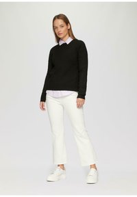 Zwarte sweater over een licht gestreept shirt, witte flared jeans en witte platform sneakers. De outfit heeft een losse pasvorm en een casual ontwerp.