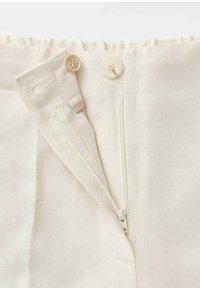 Light beige pants with elastic waistband, zipper fly partially open, button closure, and small inner button for extra fastening.
