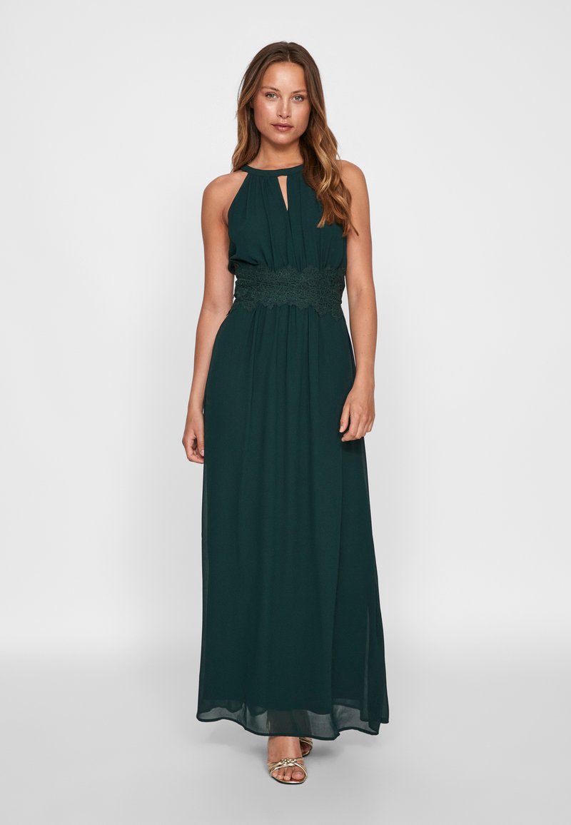 Μάξι φόρεμα σε σκούρο πράσινο, με λαιμόκοψη halter, λεπτομέρεια με δαντέλα στη μέση και ρέον ύφασμα από σατέν. Μικρό σκίσιμο στο μπροστινό τελείωμα.