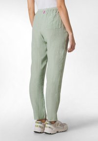 Lichtgroene linnen broek met een relaxed fit, elastische tailleband en een achterzak. Gemaakt met grijze sneakers met gele accenten.
