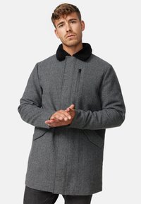 Abrigo de mezcla de lana gris con un cuello de pelo sintético negro, cuenta con un bolsillo en el pecho con cremallera y bolsillos laterales, y un diseño de corte recto.