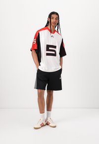 White jersey with red and black accents, large number 5, paired with black shorts and cream sneakers featuring red stripes.