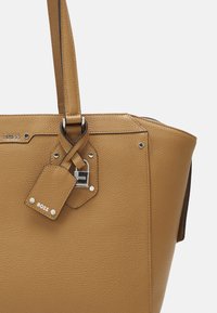 Torba na ramię w kolorze jasnobrązowym, ze skóry o fakturowanej powierzchni, srebrnymi elementami, odpinaną metką oraz usztywnionym fasonem z podwójnymi paskami.