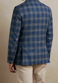 Blå rutig jacka med texturerat tyg, med en två-knaftning och ventilerad rygg. Detaljer inkluderar ljusa rutmönster.