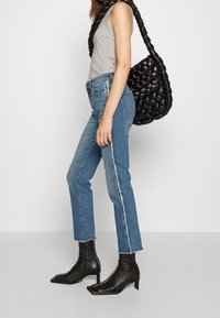 Šedý tílko, modré džíny s vysokým pasem a roztrhanými okraji, a černá pletená taška. Černé kotníkové boty s špičatými špičkami a čtvercovými podpatky.