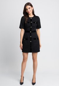Czarna sukienka z krótkimi rękawami, z przodu zapinana na guziki, z dwiema kieszeniami i złotymi akcentami. Teksturowana tkanina z dopasowanym wcięciem w talii i prostą spódnicą.