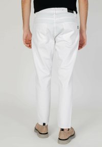 Jeans blancos con un diseño de pierna recta, que cuentan con bolsillos traseros y una etiqueta negra en la cinturilla, combinados con zapatos beige.