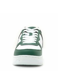 Scarpa sportiva bianca con dettagli verdi, caratterizzata da una punta arrotondata, lacci piatti, dettagli perforati e una suola in gomma testurizzata.