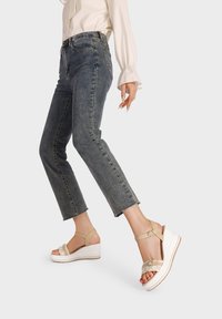 Sandali platform beige con una fascia testurizzata, cinturino alla caviglia e una suola bianca. Abbinati a jeans corti di un blu scuro.