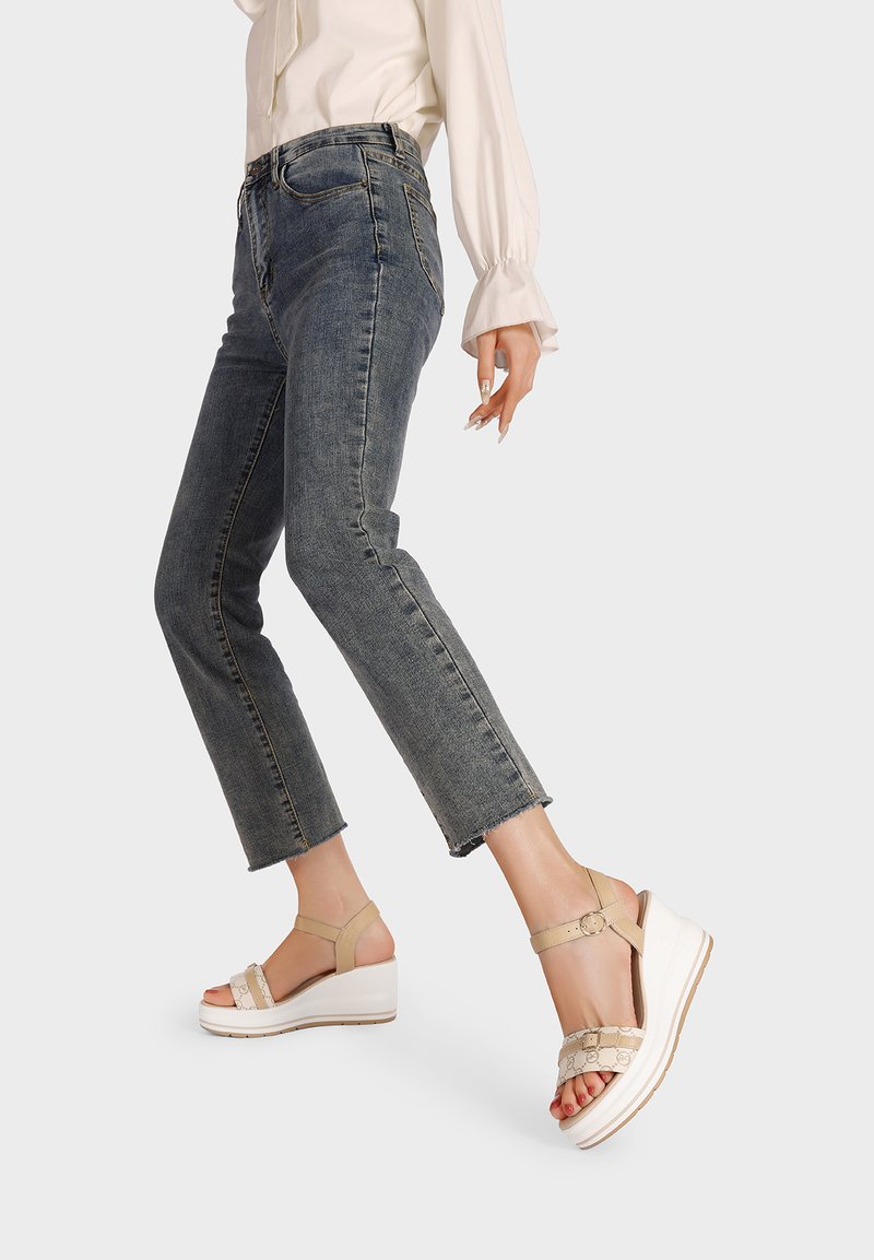 Sandali platform beige con una fascia testurizzata, cinturino alla caviglia e una suola bianca. Abbinati a jeans corti di un blu scuro.