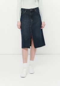 Mørk denim midi-skjørt med splitt foran, to frontlommer og knappelukking i livet. Kombinert med hvite sneakers og sokker.
