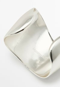 Polished silver cuff bracelet with smooth, curved edges and embossed logo "Massimo Dutti" on the inner surface. Reflective surface.