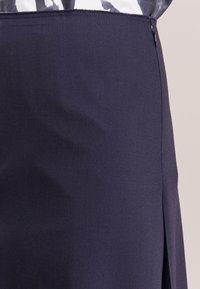 Marinblå kjol med en slät yta, som har en sidodragkedja och en diskret sprunddetalj för enkel rörelse. Ren, skräddarsydd design.