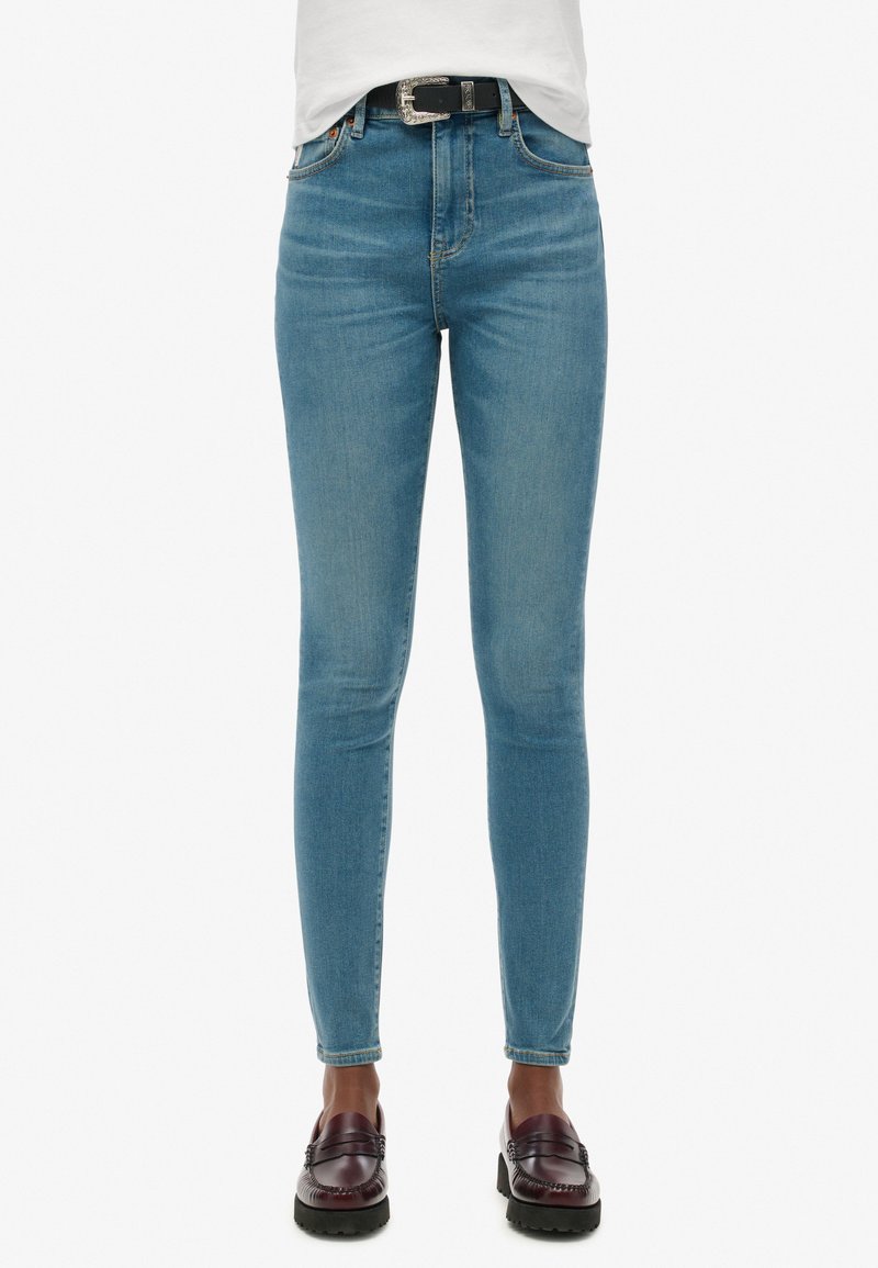 Jeans ajustados de color azul claro, confeccionados en denim, con una cintura alta, un ligero desgaste y un diseño clásico de cinco bolsillos, combinados con mocasines oscuros.