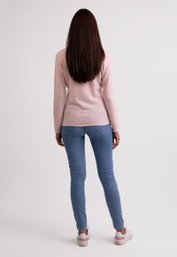 Ljusrosa långärmad topp som kombineras med blå skinny jeans och vita sneakers. Toppen har en figurnära design och mjuk textur.