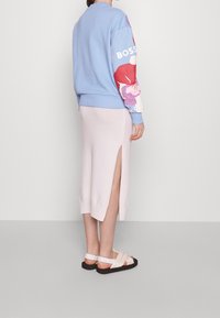 Felpa azzurro chiaro con stampa floreale colorata sulle maniche, abbinata a una gonna in maglia leggera rosa chiaro lunga fino al ginocchio, con uno spacco laterale. Sandali neri e beige.
