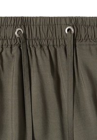 Taille élastique avec cordon sur un pantalon en tissu vert olive, avec œillets métalliques pour le cordon.