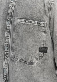 Grijze denim overhem met een knoopsluiting aan de voorkant, een borstzak en een G-Star label. Zachte textuur met een vervaagde afwerking en licht verweerde details.