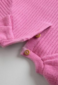 Maglione rosa a coste con una texture morbida e bottoni in legno al colletto, caratterizzato da una vestibilità rilassata e da dettagli sottili lungo i bordi.