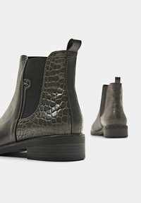 Musta nilkkurit, jotka on valmistettu sileästä nahasta ja joissa on teksturoitu krokotiilipintakuvio sivuilla, joustavat paneelit ja matala, pinottu korko.